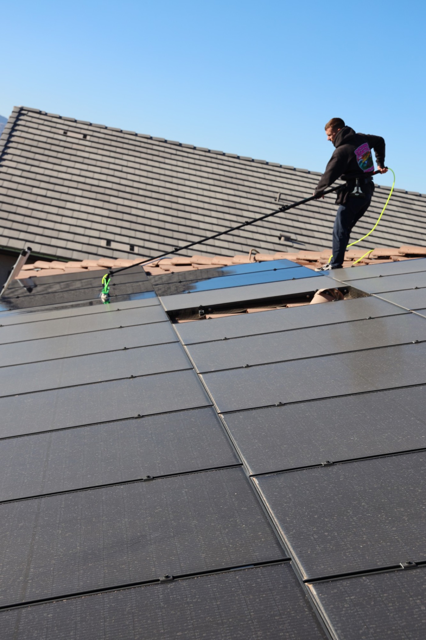 A Vero technician cleaning a rooftop solar array with a water-fed pole